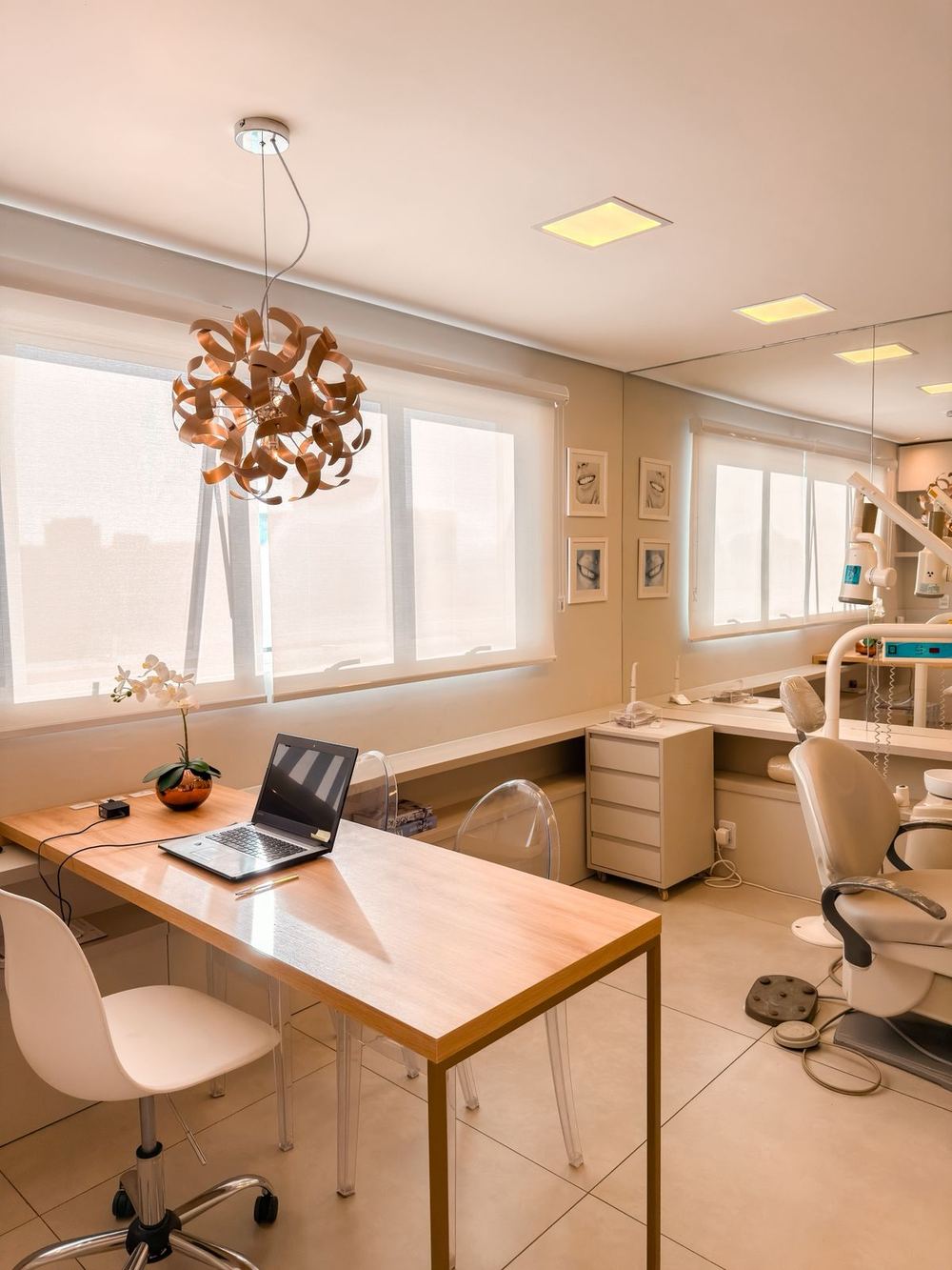 Sala de atendimento com mesa de madeira, luminária pendente e cadeira odontológica