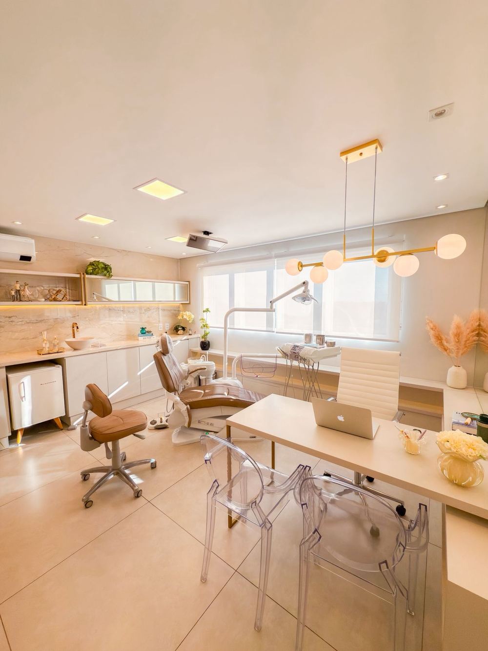 Sala de atendimento com cadeira odontológica caramelo, bancada em mármore e luminária dourada